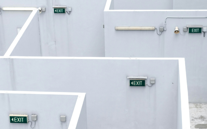 Multiple green exit signs on gray maze walls